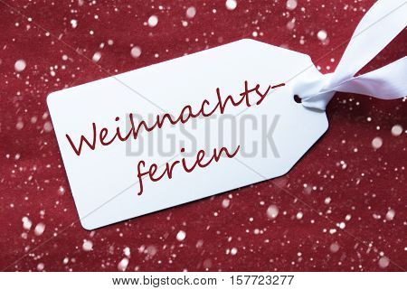 One White Label On A Red Textured Background. Tag With Ribbon And Snowflakes. German Text Weihnachtsferien Means Christmas Break
