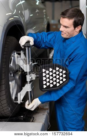 Involved in work.Professional young mechanic standing near car and adjusting automobile wheel alignment while being involved in work