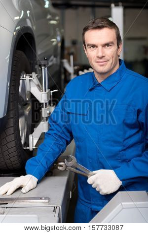 Devoted worker. Pleasant delighetd mechanic holding wrench and reparing car wheel system while workig i auto service