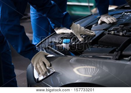 Find out break out. Professional mechanics examining engine while opening car bonnet