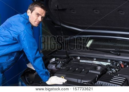 Where is break out. Professional concentrated mechanic examining engine while opening car bonnet
