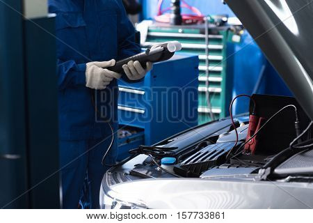 Proper data. Professional mechanic holdign special device and checking car