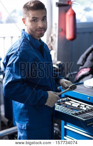 Professional attitude. Handsome concentrated man holding wrench and lookign at you while working in auto center