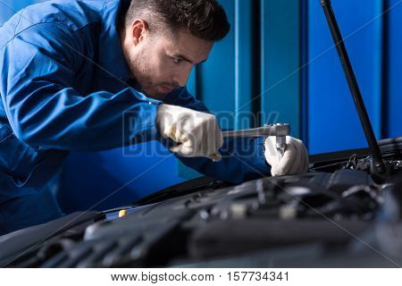 Serious worker. Professional mechanic using wrenches and repairing car engine while working