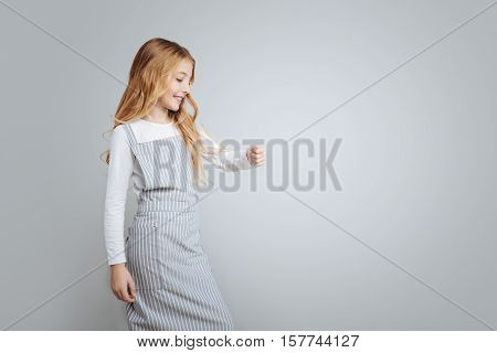Upbeat mood. Positive gelighted cute little girl smiling and cooking her dish in the on the cooker while standing isolated on grey background