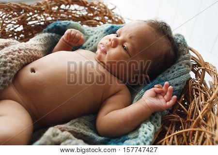 African newborn kid lying in wicker cradle close-up. Adorable child rest in nest. Naked innocent baby picture