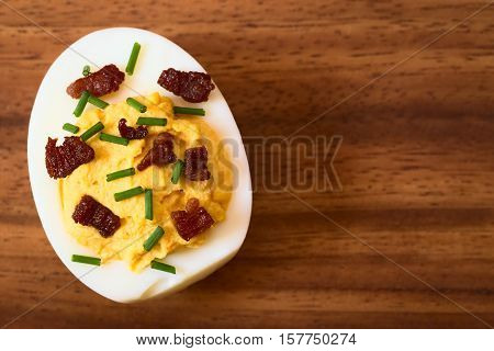 Deviled egg with bacon and chives photographed overhead on wooden plate with natural light (Selective Focus Focus on the top of the egg yolk)