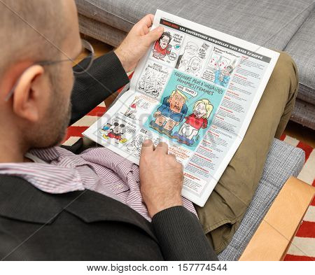 PARIS FRANCE - NOV 12 2016: Man reading Charlie Hebdo magazine on after Donal Trump elections as USA President -admiring Trump Clinton cartoon