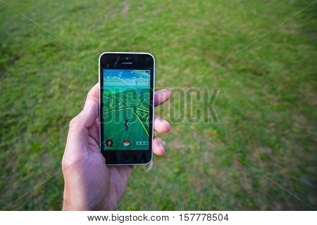 Buenos Aires, Argentina - Nov 11, 2016: Apple iPhone 5c held in one hand showing its screen with Pokemon Go application. Grass on the background.