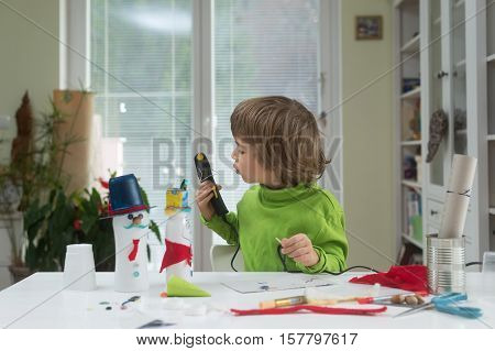 Little boy being creative making homemade do-it-yourself toys out of yogurt bottle and paper using hot melt glue gun. Supporting creativity learning by doing hand crafts.