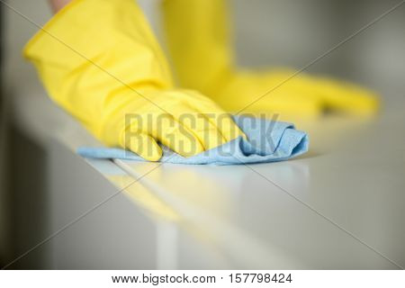Close up of hands in rubber protective yellow gloves cleaning the white surface with a rag. Home, housekeeping concept