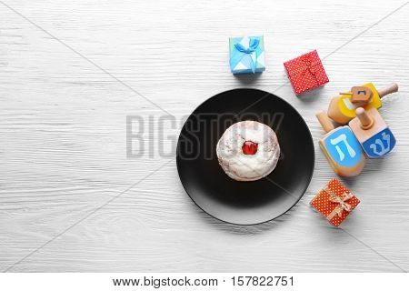 Composition of tasty donut, dreidels and presents for Hanukkah on wooden table