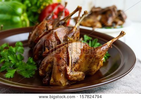 Roasted quail on a spit. Serving on a ceramic plate with greens. Close-up. Holiday menu.