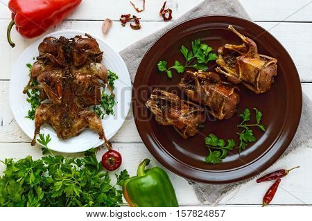 Roasted quail on a spit. Serving on a ceramic plate with greens. The top view. Holiday menu.