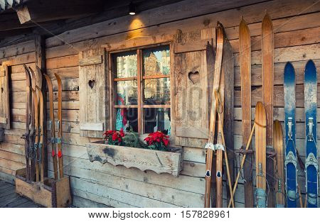 Wooden Skis Stand Near The Wall Of An Old House With A Window Which Blooms Puansetiya