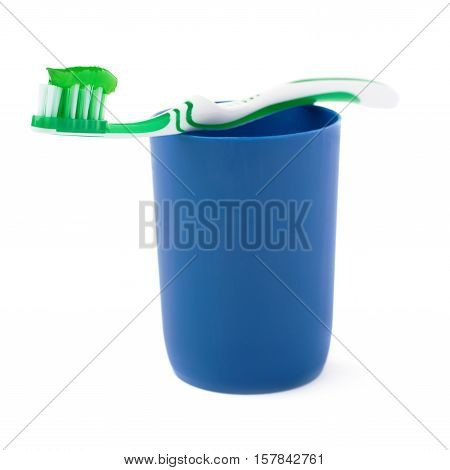 Green single toothbrush with paste lying on blue plastic cup isolated over white background