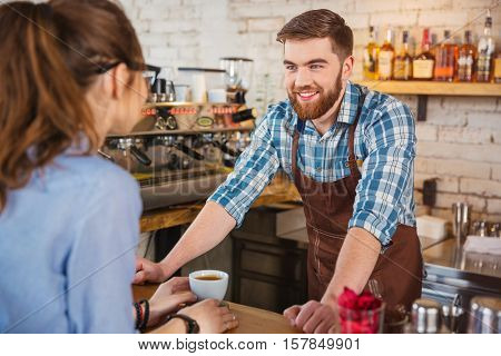 Cheerful bearded barista talking with young woman in coffee shop