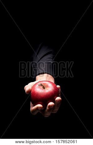 Delicious fruit. Close up of mans hand holding a red big apple and standing on black background while demonstrating it.