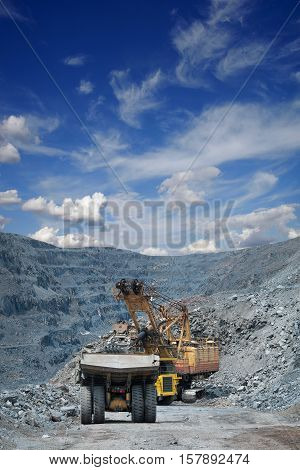Heavy mining dump trucks are being loaded with iron ore on the opencast mining on a sunny day