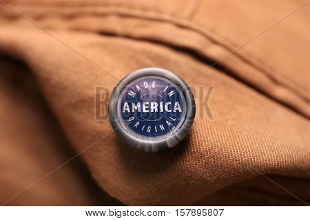 Button with text MADE IN AMERICA ORIGINAL on garment, closeup. Manufacturing quality concept.