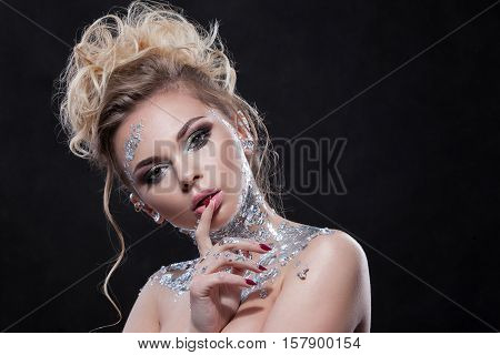 Beauty woman with beautiful makeup and silver body. Blond hair wavy hair clear skin beautiful face. Portrait shot in studio on a black background.