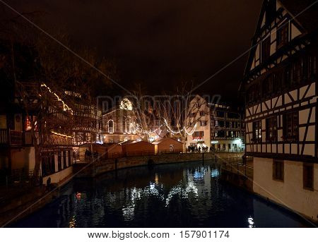 STRASBOURG FRANCE - DEC 6 2016: Christmas market in Place Benjamin Zix with its reflection in the Ill river at dusk with Christmas stalls and people shopping drinking mulled wine