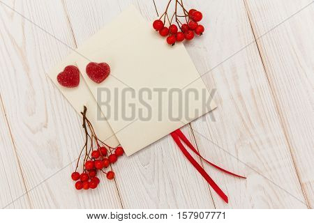 Empty envelopes with red rowan and stripe.Two red hearts jujube.White wooden table.Mokup with empty space.Top view