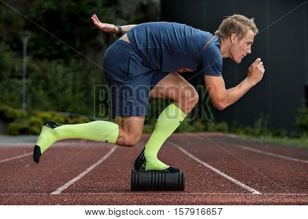 Fitness guy doing balance exercises on foam roller on an athletics track