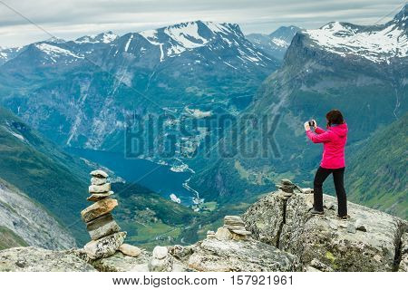 Tourism vacation and travel. Female tourist taking photo with camera enjoying Geiranger fjord and mountains landscape from Dalsnibba Plateau viewpoint Norway Scandinavia.