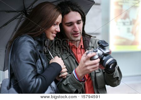 Giovane coppia sotto l'ombrello, guardando fotocamera digitale SLR, sorridente. Messa a fuoco selettiva.