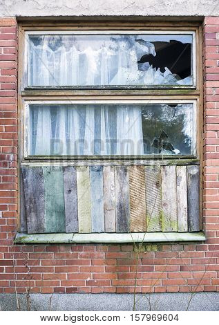 Window boarded up by wooden panels in an old red brick house with beat all glass
