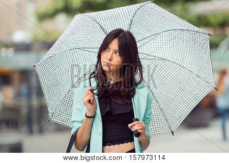 Thinking asian girl city portrait. Serious sexy woman outside with umbrella and glasses in casual business suite. Beautiful young mixed race Asian Caucasian woman.