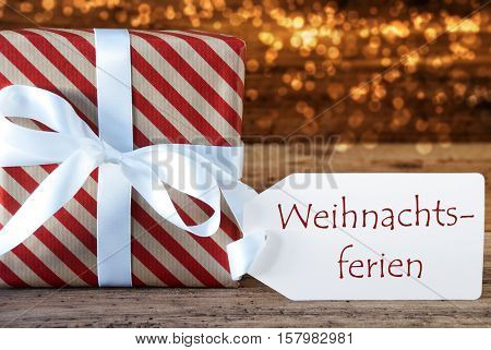 Macro Of Christmas Gift Or Present On Atmospheric Wooden Background. Card For Seasons Greetings Or Congratulations. White Ribbon With Bow. German Text Weihnachtsferien Means Christmas Break