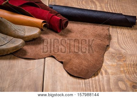 Leather in rolls and shoe lasts on wooden background. Leather craft. Copy space. Workplace for shoemaker.