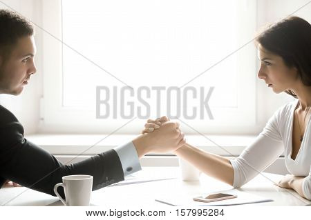 Side view portrait of man and woman armwrestling, exerting pressure on each other, looking eyes in eyes, struggling for leadership. Business, society concept photo