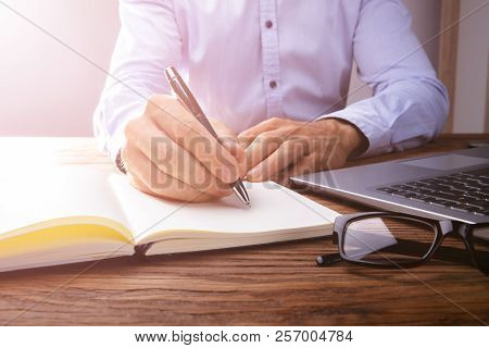 Person's Hand Writing On Black Notebook