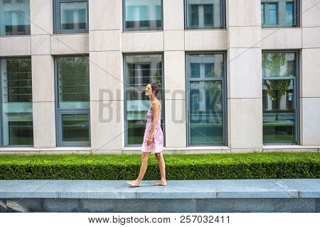 A Barefoot Woman Walks Along A Stone Border. The Brunette Is Walking Along The Street. A Slender Gir