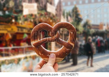 The Girl Is Holding A Traditional German Pretzel In Her Hand. Christmas Market In The Background.