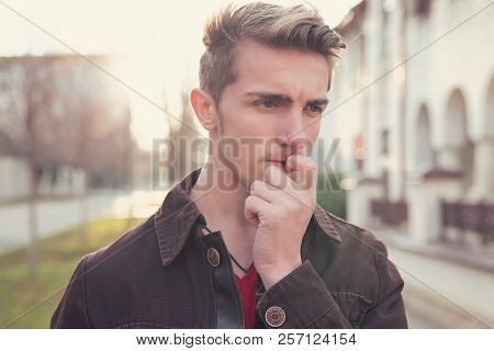 Young Preoccupied Man In Doubts Biting Nails And Looking Away While Standing On Street