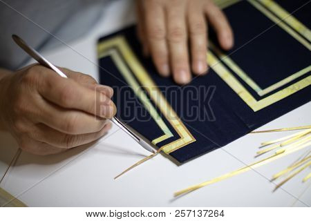 Book Binder Hand Working A Pattern On The Blue Cover Of A Hardcover Book In His Workshop In A Close 