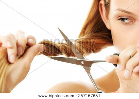 Attractive young woman is cutting her long natural hair.