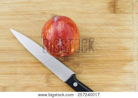 A Knife Lays Next To An Amigo Pluot Fruit On A Wood Chopping Board