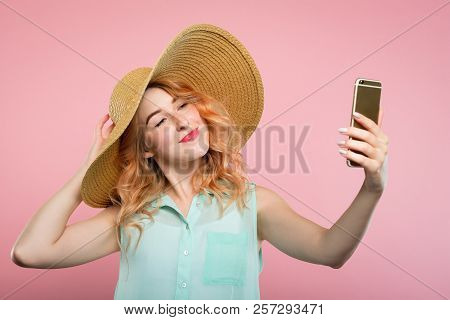 Selfie And Self Adoration. Young Stylish Woman In A Big Sunhat Taking A Photo Of Herself Using Mobil