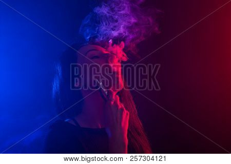 Portrait Of Asian Woman Smoking Vape Or E-cigarette In Neon Light At Black Background.