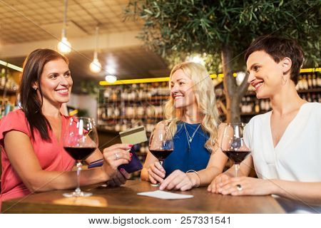 leisure, cashless payment and lifestyle concept - happy women with credit card paying bill at restaurant or wine bar