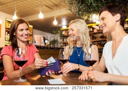 leisure, payment and lifestyle concept - happy women with money in wallet paying bill at restaurant or wine bar