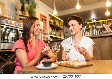 leisure, people and lifestyle concept - happy women eating snacks at wine bar or restaurant