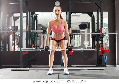 Girl With A Ponytale Wearing Pink And Black Professional Sportswear Squatting With An Iron Barbell A