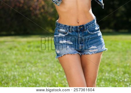 Part of the body, front view torn blue jeans shorts for women on the background summer park