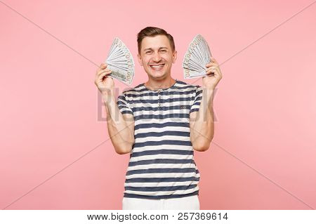 Portrait Of Smiling Excited Young Man In Striped T-shirt Holding Bundle Lots Of Dollars, Cash Money,